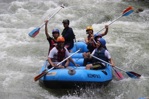 A group of people wearing safety gear raising their paddles during a white-water rafting trip.