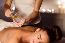 A therapist pouring massage oil onto her hand before treating a woman at a spa.