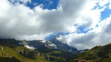A jagged mountain peak partially obscured by thick, white clouds under a bright blue sky.