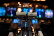 Flight deck thrust levers positioned in front of illuminated instrument display panels in an aircraft cockpit.