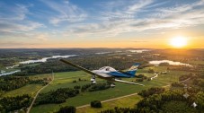 Small aeroplane flying over a scenic countryside landscape during a bright sunset.