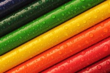 Close-up of brightly coloured pencils arranged diagonally and covered with water droplets.