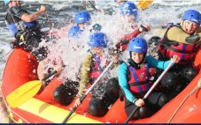 A group of people wearing helmets and life jackets white-water rafting in an inflatable boat.