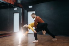 A couple practicing a contemporary dance routine with a supportive back bend in a studio.