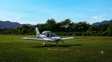 Small light aircraft parked on a grassy airfield with trees and mountains in the background.
