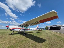 A small, white single-engine propeller aeroplane with red and blue stripes parked on a grassy airfield.