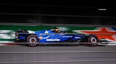 A blue Formula One race car driving along a street circuit track at night.