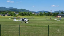 Light aircraft taxying across a grassy airfield with mountains in the background.