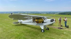 Small light aeroplane parked on a grassy airfield with two people standing nearby.